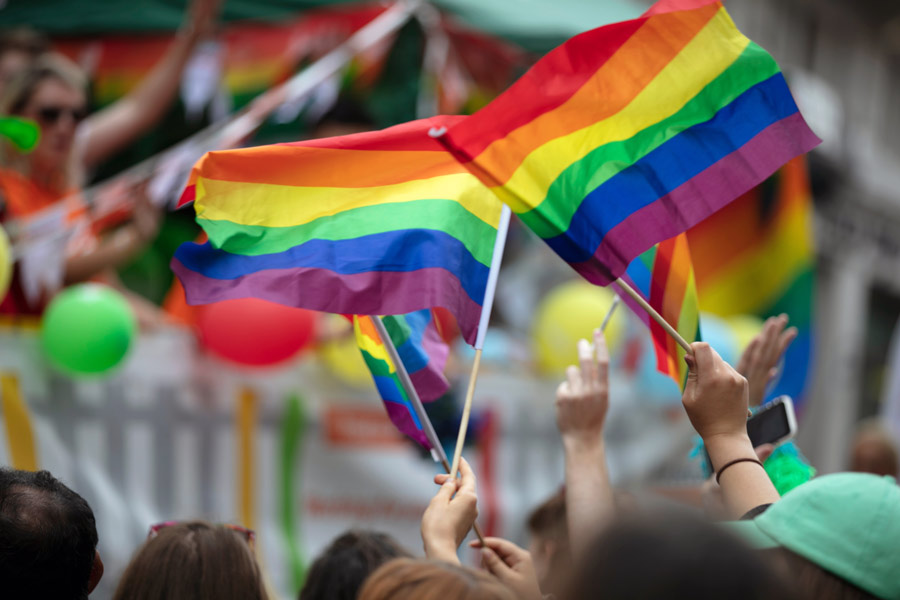 People waving rainbow flags at outdoor event.